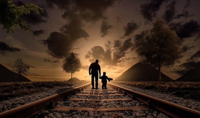 parent holding child's hand walking on railroad tracks